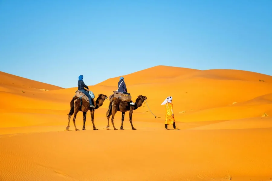 Woman in sunglasses wearing a linen outfit standing by a desert jeep
